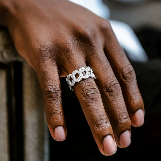 Silver-tone Cuban link ring with stone-covered links, worn on a dark-skinned hand in an angled close-up