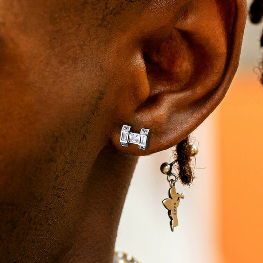 Silver-tone H-shaped stud earring worn on an ear beside a gold-tone dangling charm
