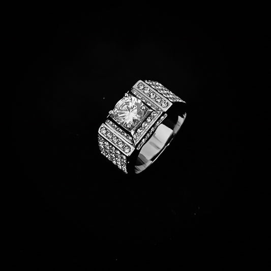 Silver-tone band ring with a central stone and multi-row smaller stones, lying flat on a black background