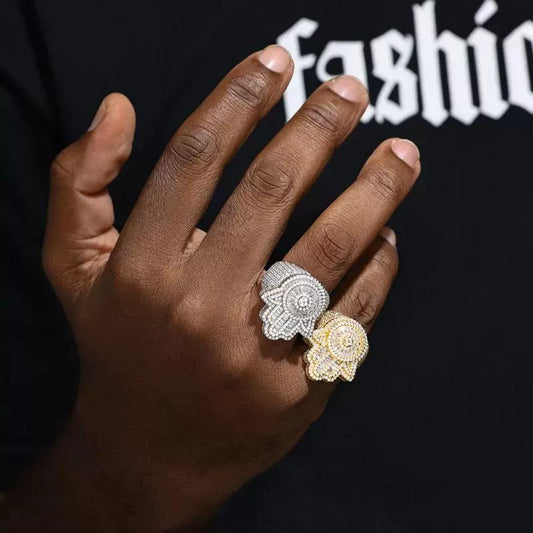 Two stacked rings with Hamsa motifs, one silver-tone and one gold-tone, stone-covered, worn on a dark-skinned hand