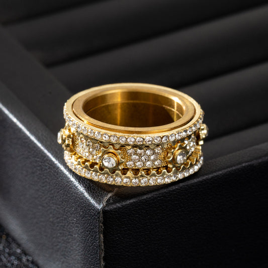 Gold-tone spinner ring with pavé-set clear stones and mechanical accents, lying flat on a black surface