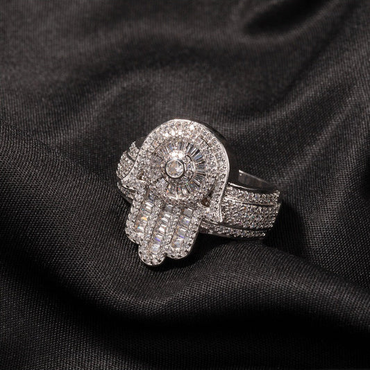 Close-up of a silver-tone sculpted ring with a Hamsa hand motif, fully stone-covered, lying flat on black fabric