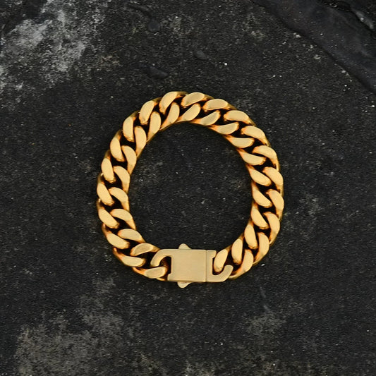 Gold-tone Cuban link bracelet with a rectangular clasp laid on a dark textured surface
