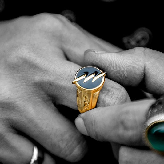 Gold-tone lightning bolt signet ring worn beside a green stone ring in a close-up hand view