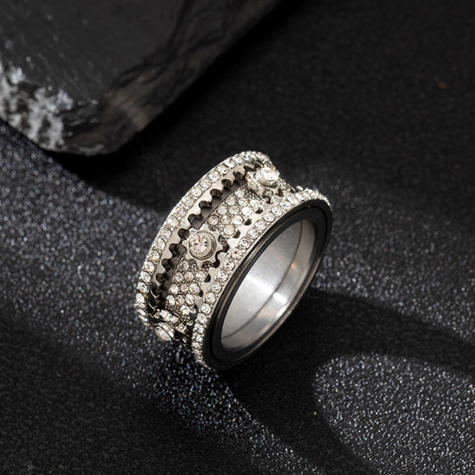 Silver-tone sculpted ring with gear-like details and full stone coverage, lying flat on a dark surface