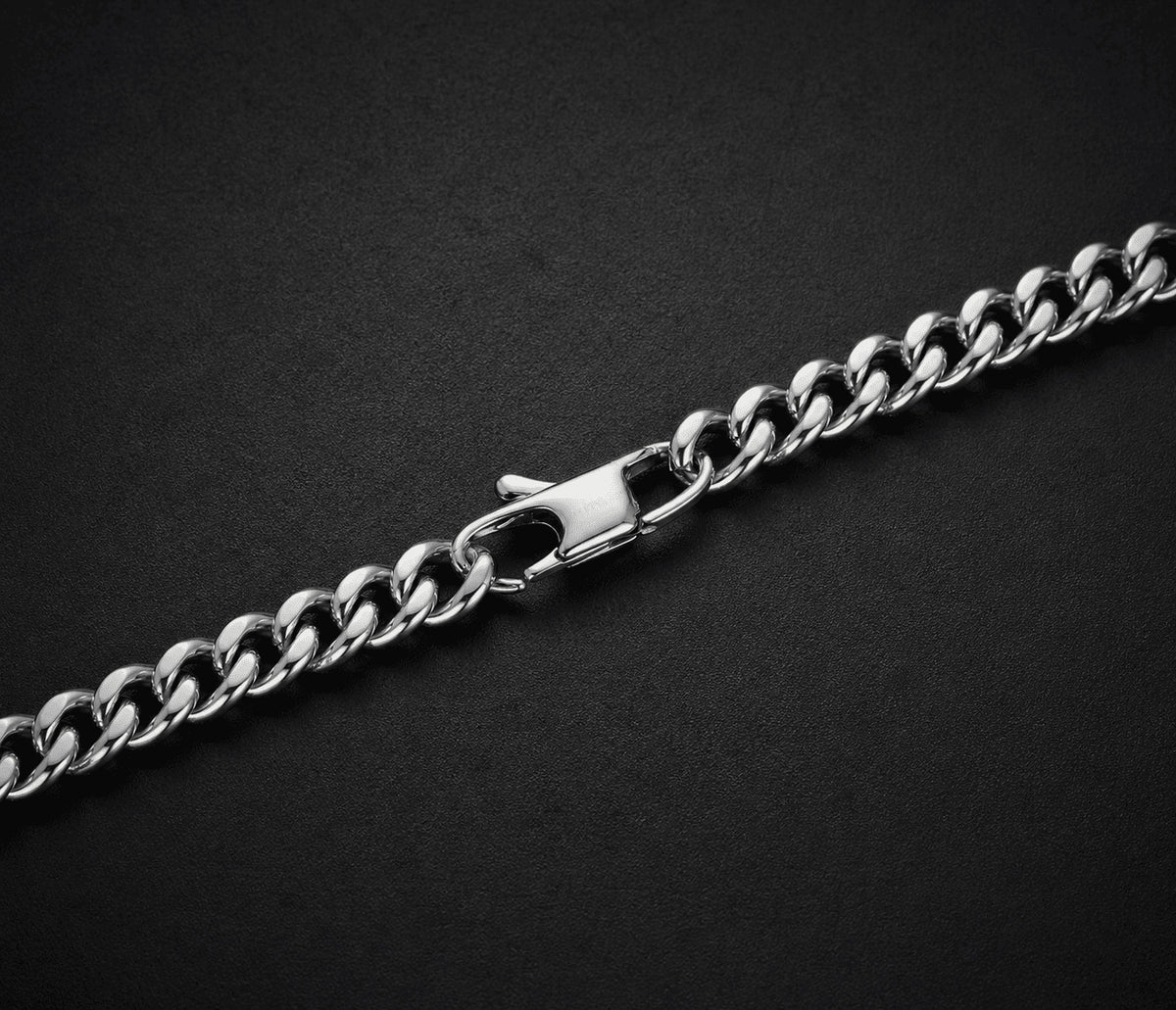 Close-up of 6MM white gold Miami Cuban link chain links and clasp laid flat on a dark textured surface