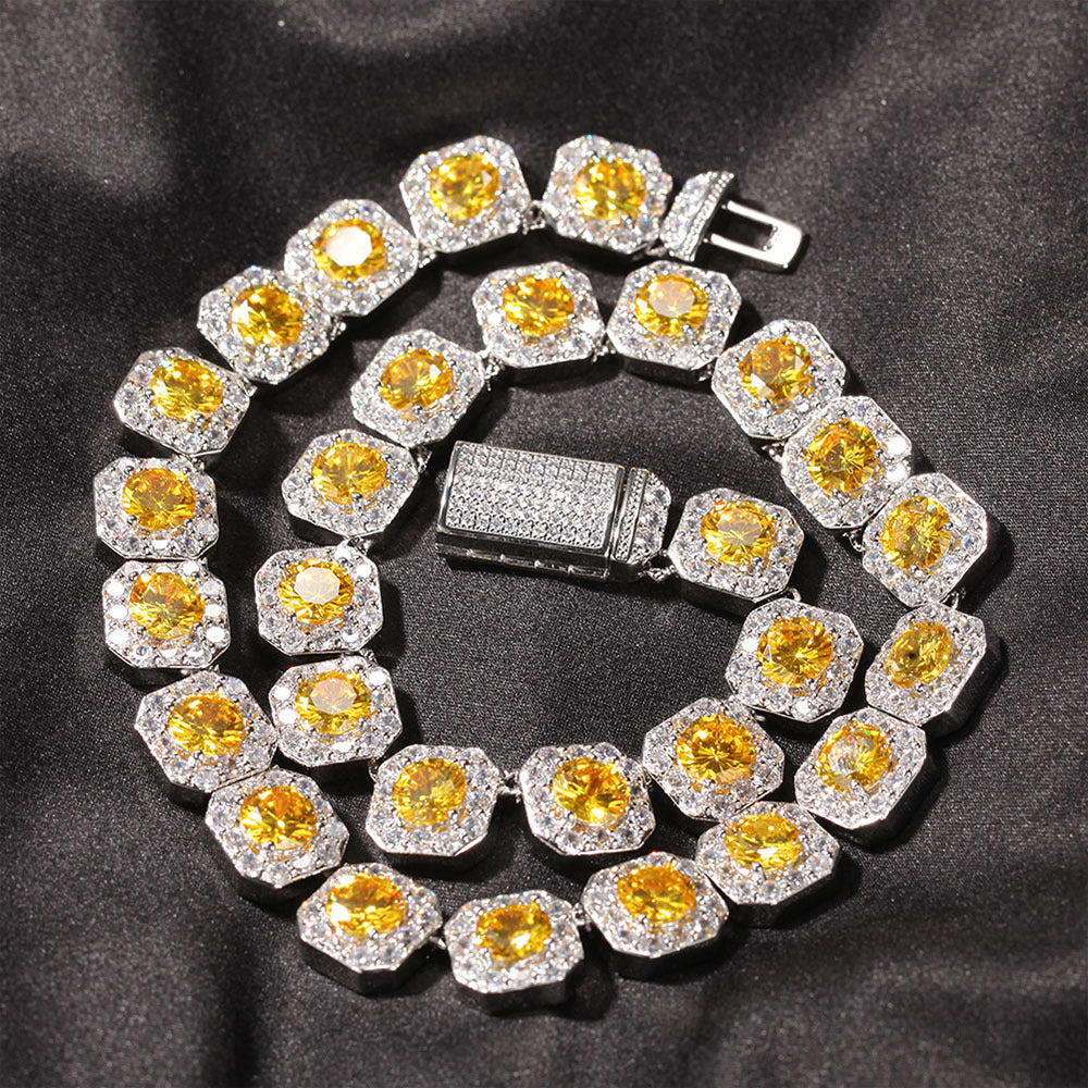 Coiled 12MM gold tennis chain on a dark textured surface showing its wide link structure with its box clasp visible