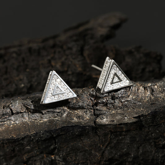 Front view of silver-tone triangle stud earrings with clear round stones on a dark textured surface