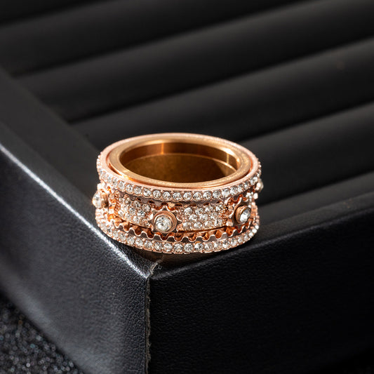 Close-up of a rose-gold-tone band ring with multi-row clear stone coverage, lying flat on a black surface