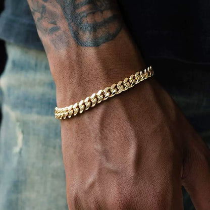 Gold-tone Cuban link bracelet worn on a tattooed wrist beside faded denim