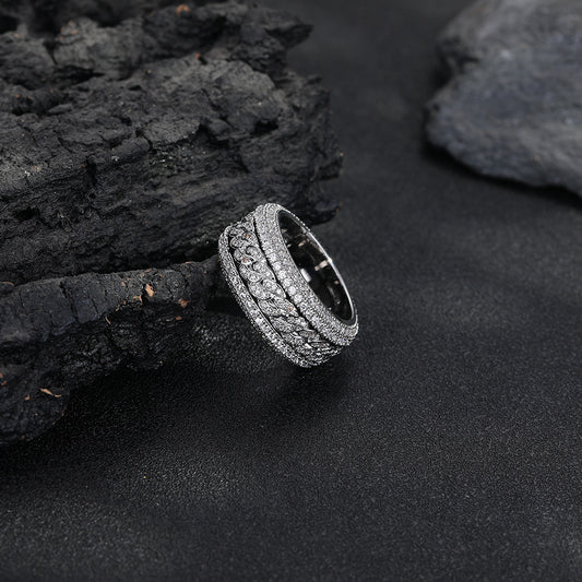 Close-up of a silver-tone band ring with intricate stone-set patterns, lying on a dark textured surface