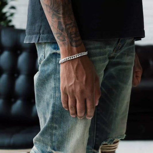 Silver-tone Cuban link bracelet worn on a tattooed wrist beside faded denim