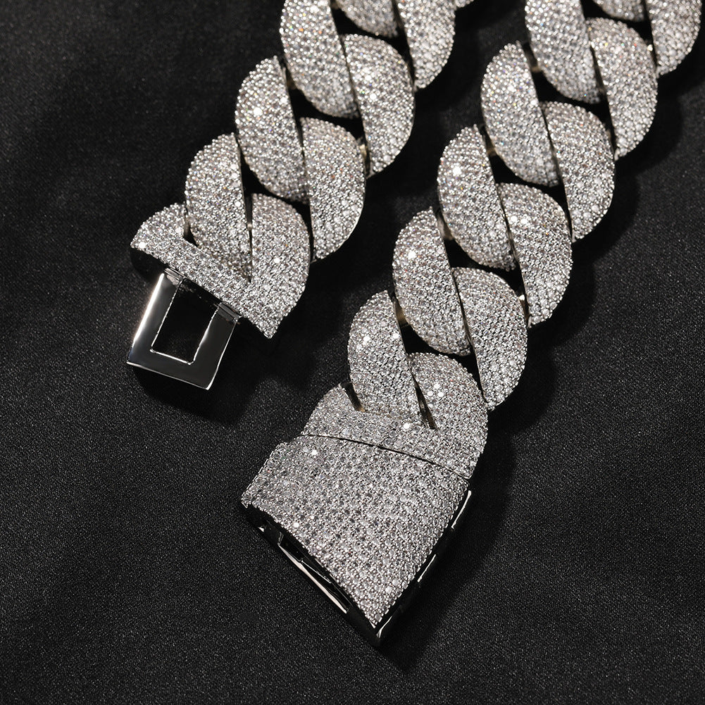 Coiled 24MM white gold Cuban link chain on a textured black surface showing clasp detail showing iced link sparkle with its