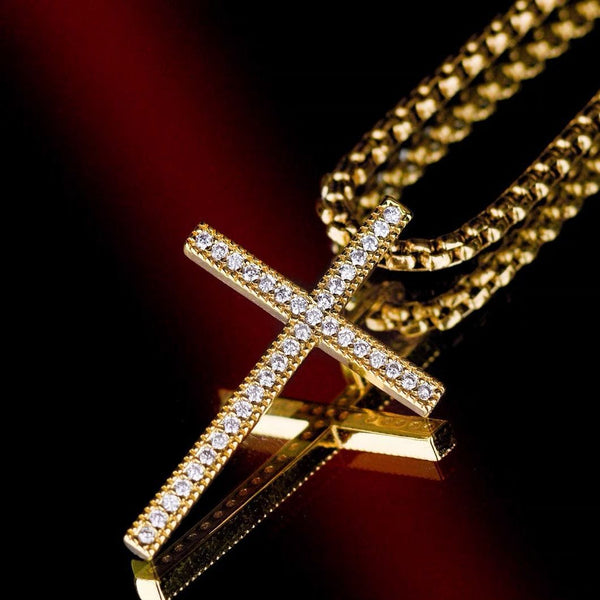 Cross pendant with slim pave cross design and a stone-covered border on a visible chain against dark textured background