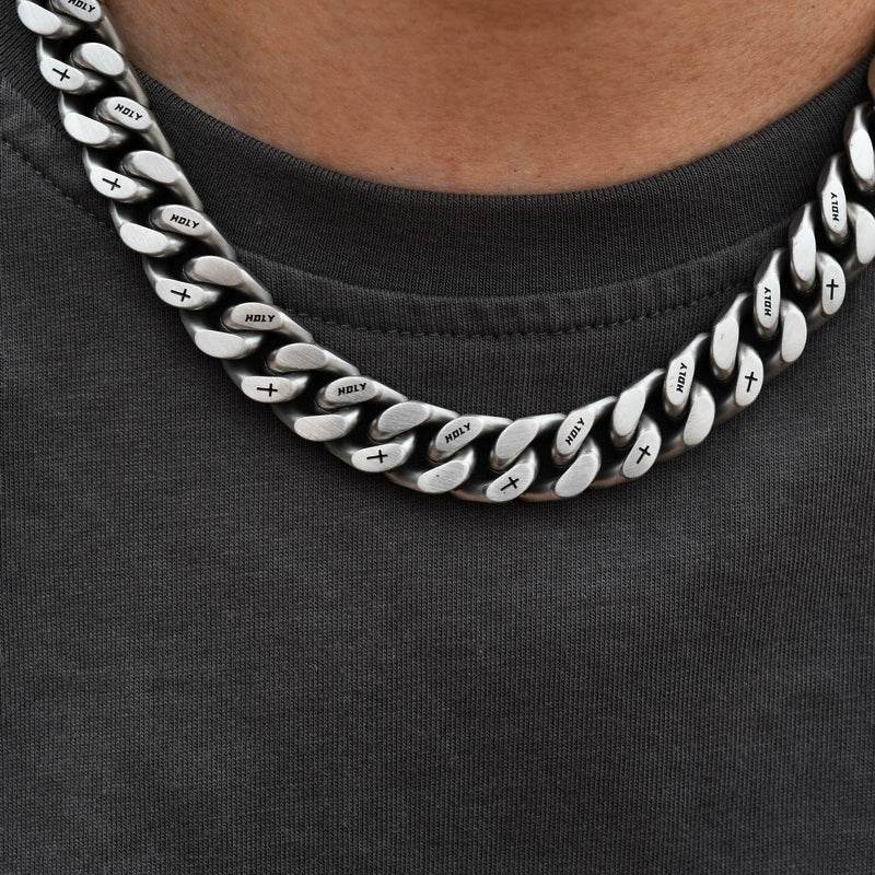 white gold Miami Cuban link chain worn around the neck over a dark gray shirt with HOLY text and cross symbols visible