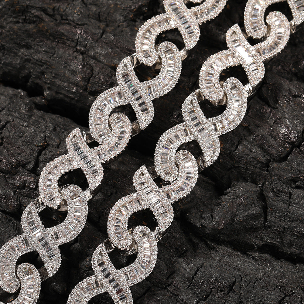 Close-up of 15MM white gold Cuban link chain links and box clasp laid flat on a dark textured surface