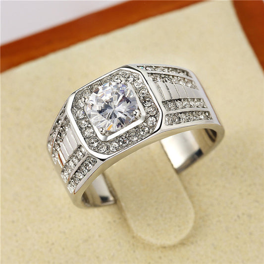 Close-up of a silver-tone band ring with a central square stone and smaller stones on the band, on a stand