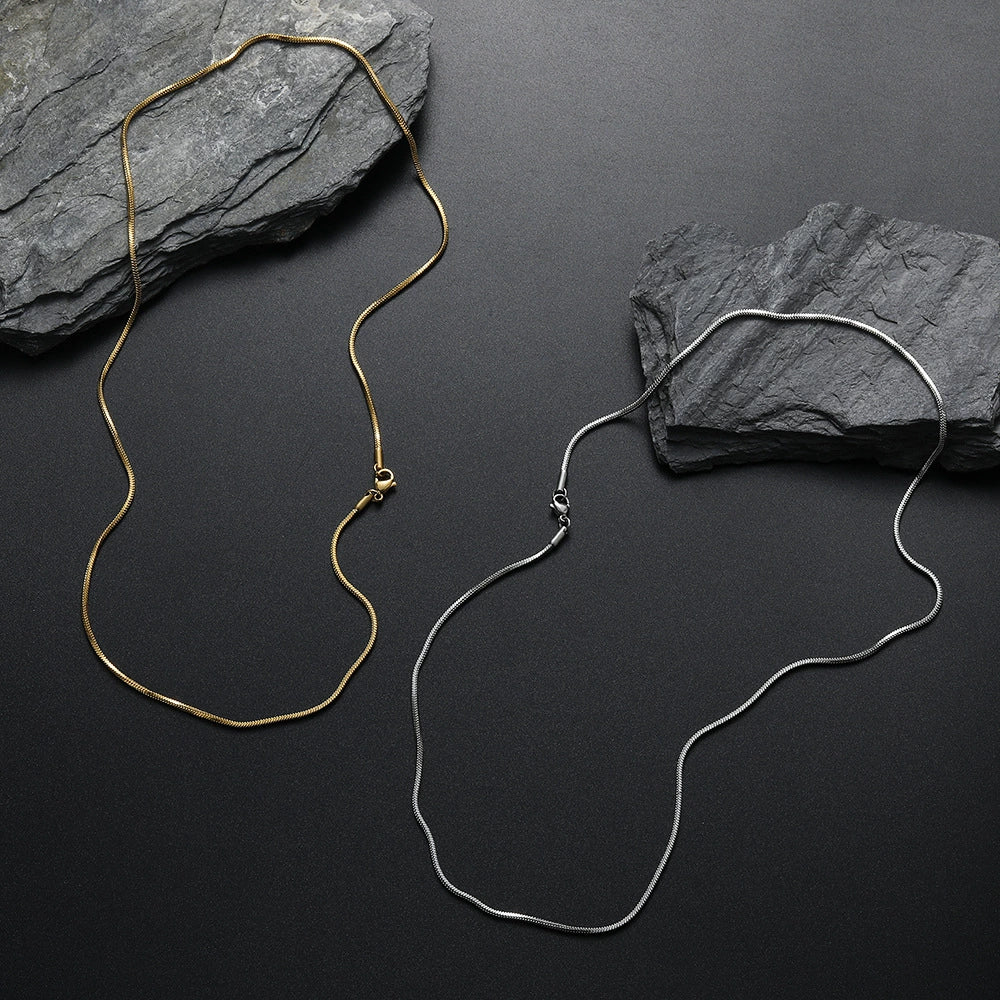 Two 2MM gold snake chains arranged in parallel on a dark textured surface