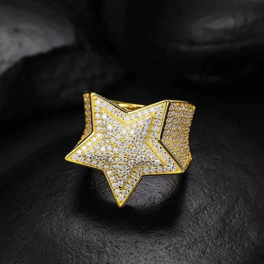 One gold-tone star ring with pavé-set stones on the star and wide band, standing upright on a dark surface