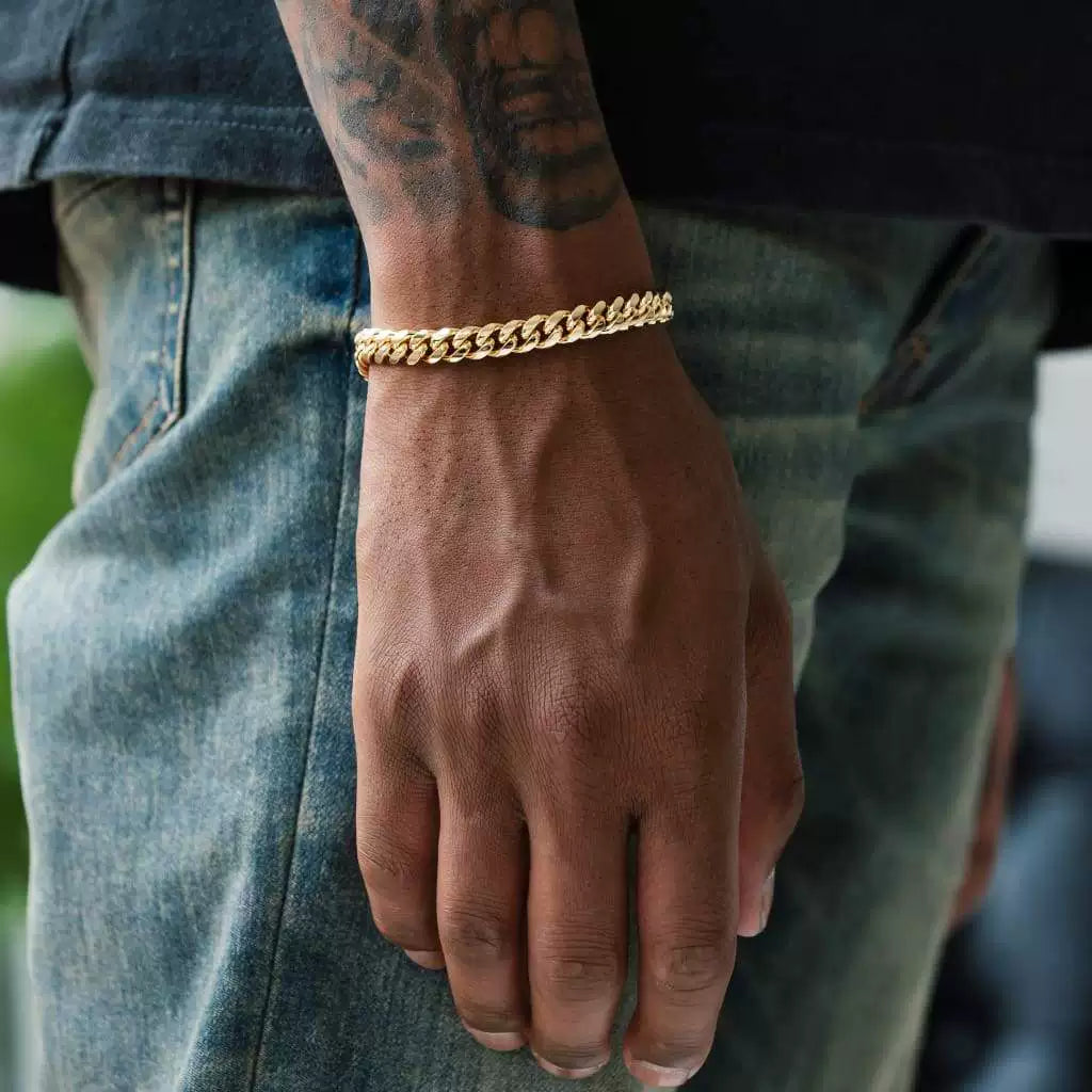 Gold-tone Cuban link bracelet worn on a tattooed wrist beside faded jeans