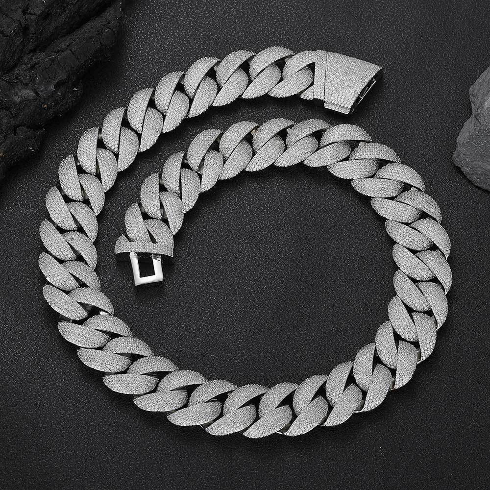 Coiled 24MM white gold Cuban link chain on a dark textured surface with its box clasp visible