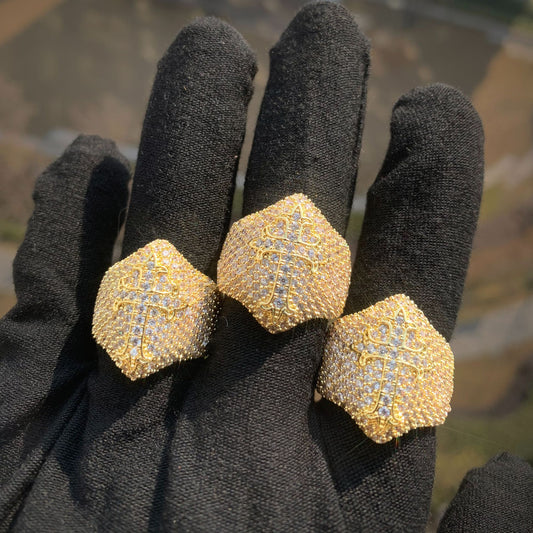 Three gold-tone cross rings with stone-covered faces worn on a gloved hand