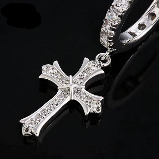 Close-up of a silver-tone cross drop earring with stone-covered hoop and cross on a black surface