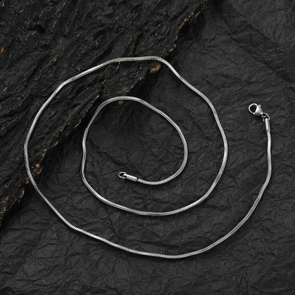 Coiled 2MM white gold snake chain on a dark textured surface with its lobster clasp visible