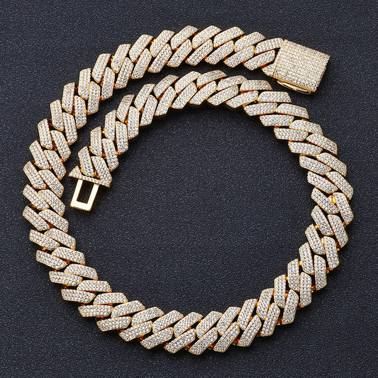 Coiled 20MM gold Cuban link chain on a dark textured surface with its box clasp visible