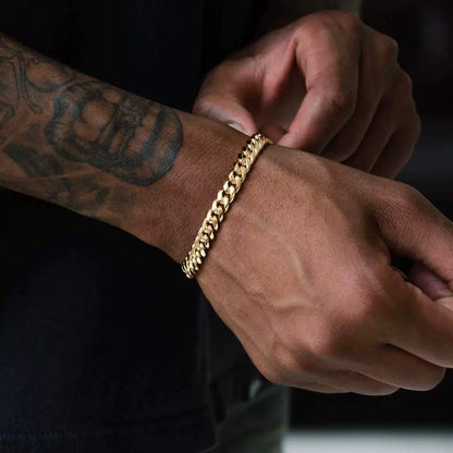 Gold-tone Cuban link bracelet worn on a tattooed wrist in a dark close-up
