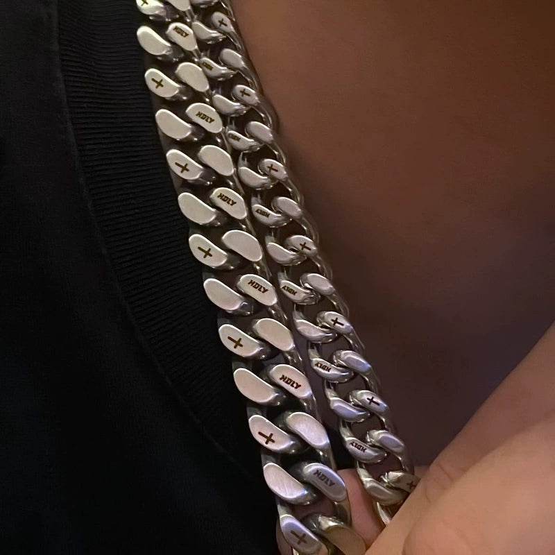 white gold Miami Cuban link chain worn around the neck on dark fabric with HOLY engraved text visible