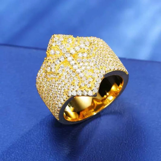 Close-up of a gold-tone cross ring with pavé stones, shown upright on a blue surface