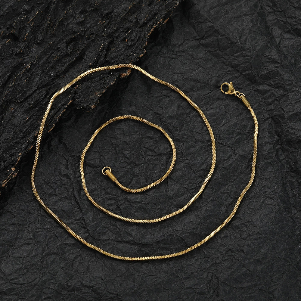 Coiled 2MM gold snake chain on a dark textured surface with its lobster clasp visible