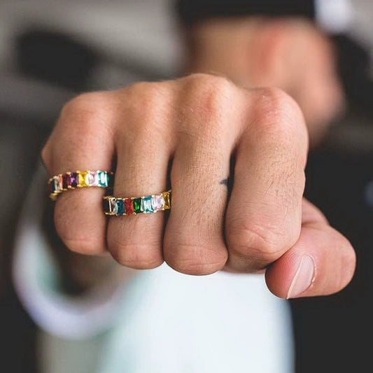 Two gold-tone band rings with multicolor rectangular stones, worn on adjacent fingers in close-up