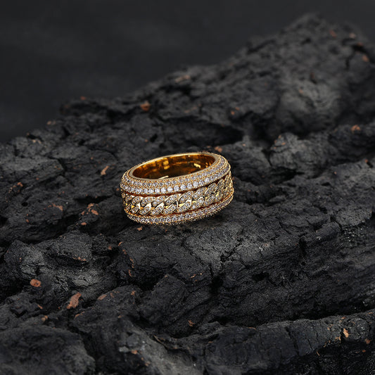 Close-up of a gold-tone Cuban link ring with stone-set edges, lying flat on a dark textured surface