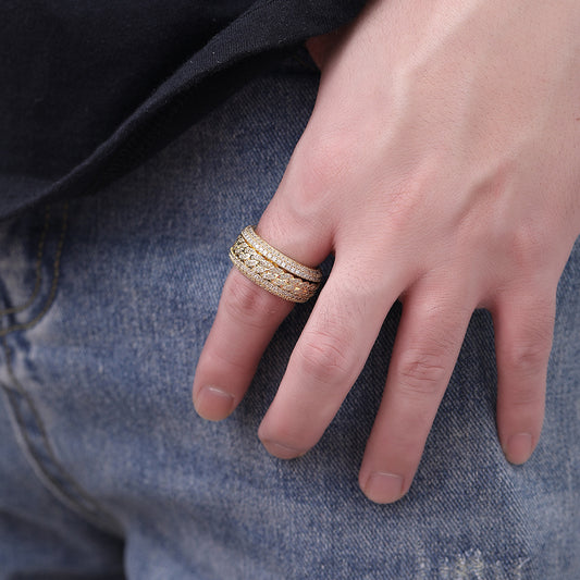 Close-up of a hand wearing three gold-tone rings with full stone coverage, stacked on a finger, against denim