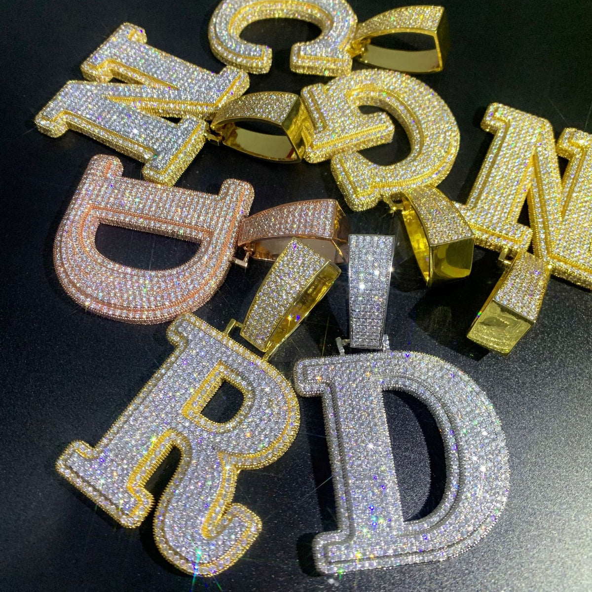 A group shot of IceGrind initial pendants including D, R, N, and G in multiple finishes. Heavyweight, hand-set custom gold initial pendant necklaces.
