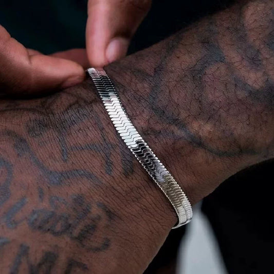 Silver-tone flat herringbone bracelet held against a tattooed wrist in close-up
