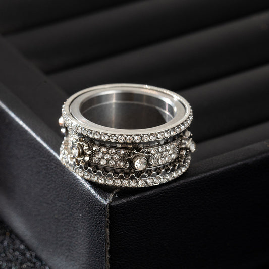 Close-up of a silver-tone band ring with multi-row clear stones and central accents, lying flat on a black surface