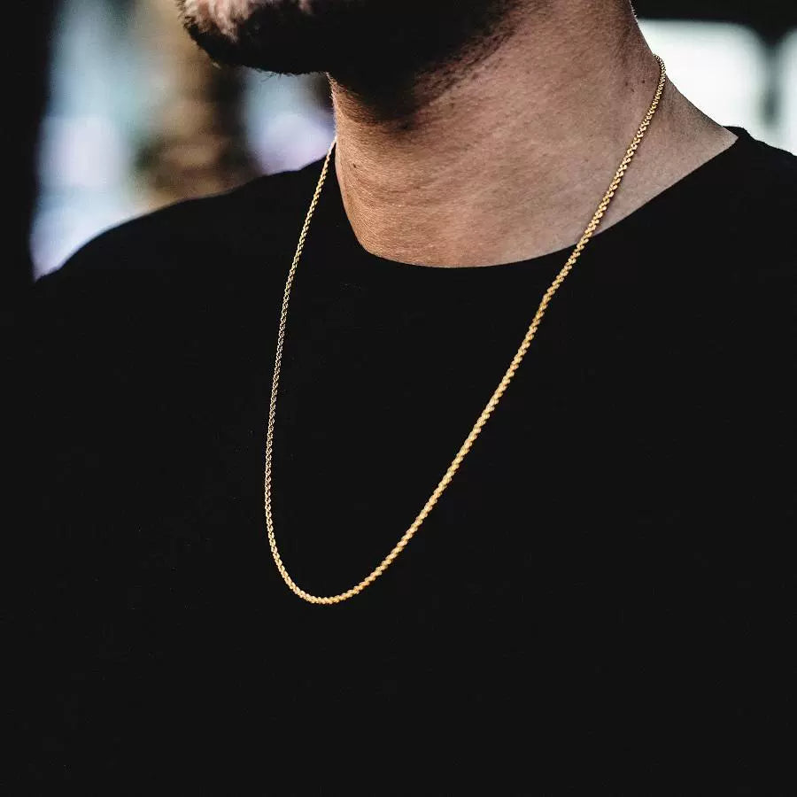 3MM gold rope chain worn around the neck in a blurred indoor setting
