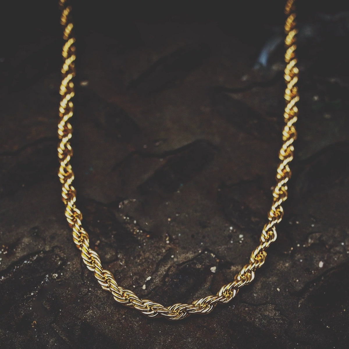 Close-up of 3MM gold rope chain links laid flat on a dark textured surface