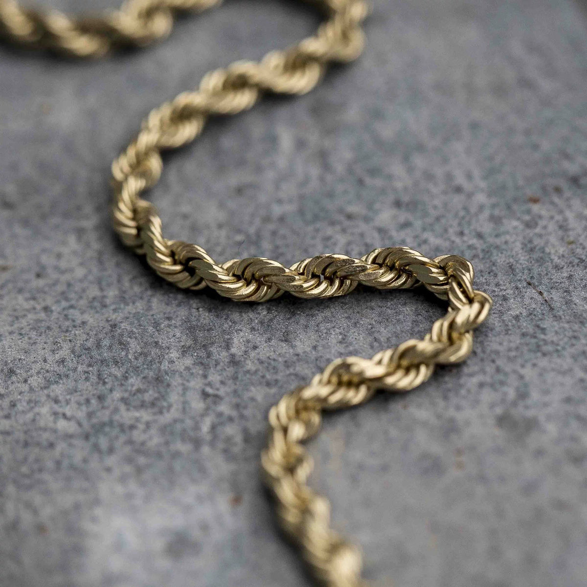 Curved 3MM gold rope chain laid on a textured gray surface